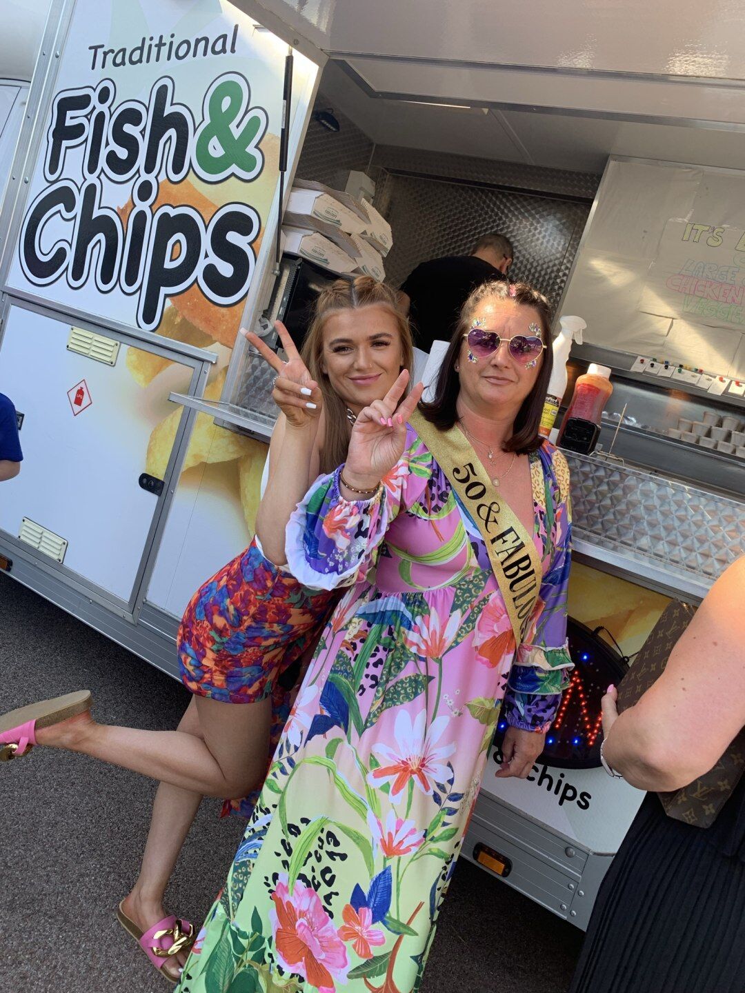 Birthday girl in a '50 & Fabulous' sash with a guest, posing in front of the DB's fish and chip van